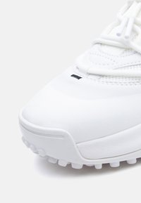 Άσπρο αθλητικό παπούτσι με κομψό σχεδιασμό, υφασμένο επάνω μέρος, ομαλή μύτη και σχέδιο στην σόλα για καλύτερη πρόσφυση. Τα κορδόνια είναι άσπρα και λιτά.