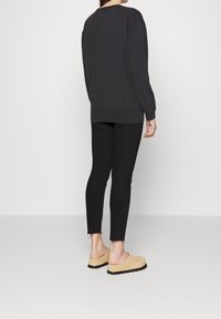 Šedá oversized mikina s žebrovanými manžetami a lemem, v kombinaci s černými skinny kalhotami střiženými nad kotníky a béžovými botami bez zavazování.