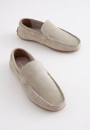 Scarpe slip-on in camoscio beige chiaro con cuciture decorative lungo i bordi e suola in gomma flessibile, caratterizzate da una texture liscia e morbida.