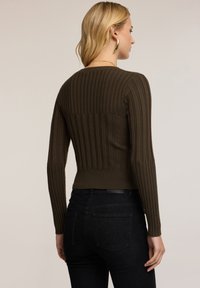 Suéter de canalé verde oliva oscuro con mangas largas, cintura ajustada y textura sutil. Llevado con jeans negros, mostrando vista posterior.