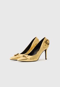 Gold metallic high heels with pointed toes, a decorative buckle detail, and a slim stiletto heel. Smooth texture and sleek design.