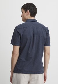 Cămașă cu mânecă scurtă, de culoare albastru închis, dintr-un material ușor, cu guler clasic, spate cu yoke și o croială lejeră.