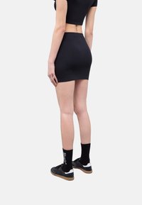 Top corto nero e gonna mini vista dal retro. Calzini neri alla caviglia e scarpe con un accento bianco. Tessuto liscio, vestibilità aderente.