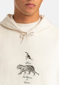 Cream hoodie with a drawstring, featuring black illustrations of a tiger and a bird, alongside the text "River" and "The Balance of Opposites."