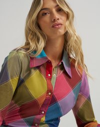 Camicia a quadri multicolore con design a bottoni, caratterizzata da una varietà di colori tra cui verde, rosso e viola, dettagliata con cuciture bianche.