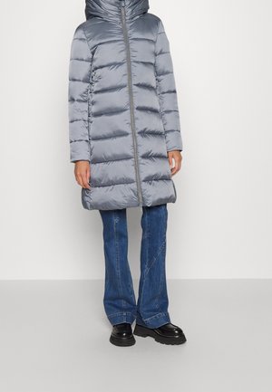 Person wearing shiny gray padded coat with hood, blue denim jeans, and black chunky shoes, standing against plain light background.