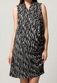 Schwarz-grau gemustertes Kleid mit ärmellosem Design, das eine drapierte Textur und eine lockere Passform aufweist, geeignet für den legeren Alltag.