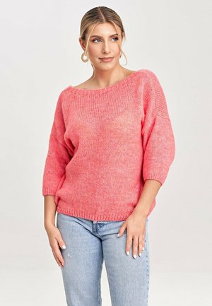 Różowy sweter z dzianiny z dekoltem w łódkę i rękawami 3/4. Charakteryzuje się luźnym krojem i ściągaczem na dole, zestawiony z jasnymi dżinsami.