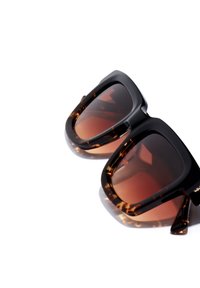 Ochelari de soare tortoiseshell negri și maro, cu un cadru robust și lentile degradate. Prezintă margini netede și un design larg, pătrățos.