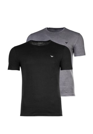 Giovane uomo che indossa una semplice maglietta grigia a maniche corte con un piccolo logo nero sul petto sinistro e pantaloni beige chiaro.