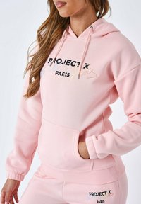 Felpa rosa chiaro con cappuccio regolabile, tasca frontale e ricamo "PROJECT X PARIS" in lettere nere e multicolori. Tessuto morbido.