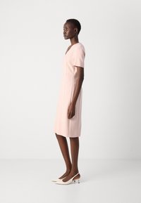 Light pink dress with short sleeves and a V-neck, featuring a fitted silhouette and knee-length hem. Worn with white pointed-toe heels.
