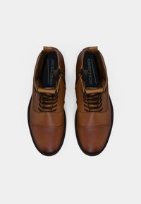 Par de botas de tobillo de cuero marrón con cordones negros, cremallera lateral y plantillas de marca "JACK & JONES", mostradas desde arriba sobre un fondo blanco.