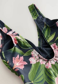Bloemend badpak met roze lelies en groene bladeren op een donkermarine achtergrond. Gemaakt van rekbare stof met dunne bandjes en een ronde hals.