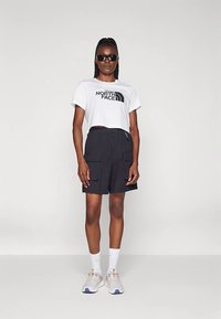 Valge lühendatud t-särk musta logoga, lahtised tumedad cargosärgid, päikeseprillid ja heledat halli värvi tossud oranžide detailidega. Stiilne ja vabaaja rõivastus.