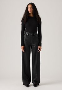Zwarte langarmsgemouwen top, gecombineerd met hoge taille, wijde zwarte broeken. Gladde textuur, minimale details en een getailleerde silhoutte.