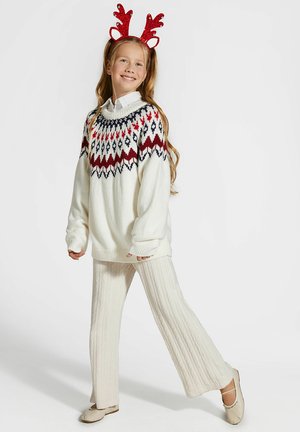 Biały dziergany sweter z wielokolorowym wzorem na karczku, zestawiony z kremowymi prążkowanymi spodniami i neutralnymi balerinami. Czerwona opaska z rogami jelenia.