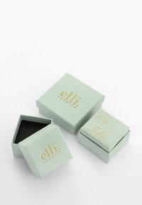 Mintunvihreitä lahjalaatikoita, joissa on kultaiset kirjainmerkinnät. Yksi laatikko on avoin, ja sen sisusta on musta. Muut laatikot ovat suljettuja ja niissä on siisti design.