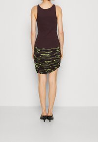 Svart linne som matchar en svart kjol med rynkningar och gröna abstrakta mönster, kompletterat med svarta högklackade skor.