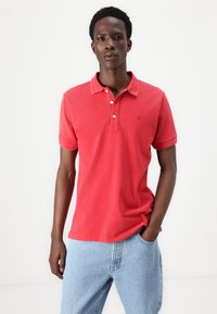 Polo shirt en coton rouge à manches courtes, avec patte de boutonnage à trois boutons et logo discret. Assorti à un jean en denim bleu clair. Design simple et décontracté.