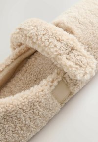 Béžová pantofle s texturovaným, nadýchaným povrchem, měkkou podšívkou a textilním páskem. Design je jednoduchý a nazouvací.