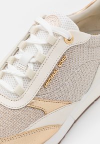 Baskets Michael Kors blanches et beiges en tissu mesh, lacets blancs, détails dorés du logo et surpiqûres en cuir.