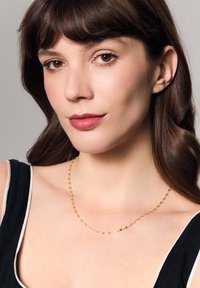 Złoty naszyjnik z łańcucha z owalnymi ogniwami o gładkiej fakturze, noszony na odkrytym obojczyku, w zestawieniu z czarną bluzką z białymi akcentami.