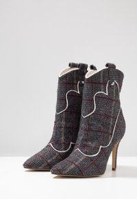 Gray plaid ankle boots with a pointed toe, textile material, scalloped white trim, and a stiletto heel. Features a checkered pattern.