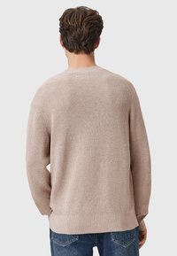 Jasno beżowy sweter z dzianiny o teksturowanym wzorze, okrągłym dekolcie i luźnym kroju. Szczegóły z prążkowanymi mankietami i dołem. Nosi się go na niebieskie dżinsy.