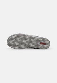 Semelle de chaussure en caoutchouc gris avec un motif texturé et un accent de logo rouge. Le design a une forme légèrement courbée pour un ajustement ergonomique.