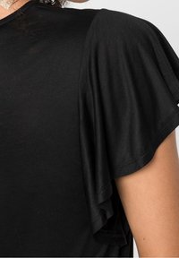 Close-up of a black flutter sleeve on a person’s arm, showing fabric texture and stitching details.