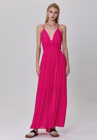 Robe maxi en tissu rose vif, dotée de fines bretelles, d'un décolleté en V plongeant et de volants en cascade sur la jupe. Design léger et fluide.