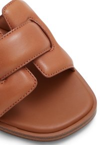 Sandale en cuir marron avec deux larges strap en cuir accentués de coutures. Design à bout ouvert et semelle plate avec une surface texturée.