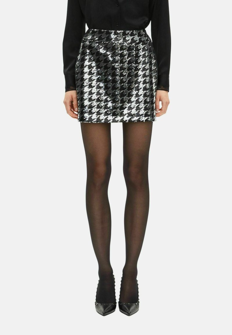 Gonna mini nera e argento con paillettes e motivo a scacchi, texture liscia e design aderente, abbinata a collant neri e tacchi.