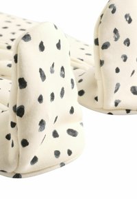 Chaussons de couleur crème avec des motifs de points noirs, fabriqués en tissu doux, avec des bords arrondis et un design rembourré pour le confort.
