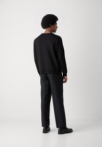Sudadera negra con cuello redondo, costuras laterales y puños acanalados. Combinada con pantalones oscuros y zapatos negros. Diseño simple, con detalles mínimos.