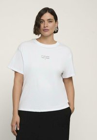 Weißes Baumwoll-T-Shirt mit Rundhalsausschnitt und kurzen Ärmeln, mit dem in Grau zentriert auf der Vorderseite aufgedruckten Text "WENN NICHT JETZT, WANN DANN".