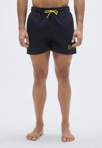 Tengerészkék úszónadrág sárga zsinórral, rugalmas derékrésszel és kis sárga logóval az oldalon. Könnyű, sima anyagból készült, térdig érő fazon.