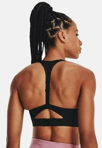 Sostenedor deportivo negro con diseño de espalda nadadora, corte decorativo y tirantes ajustables con cierre de gancho en la parte trasera.