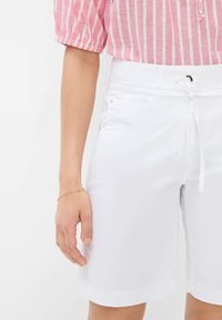 Shorts en coton blancs avec un taille élastique à cordon, poches avant et une texture lisse. Le bras du mannequin porte un bracelet délicat.