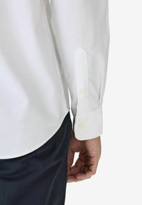 Valkoinen pitkähihaisia paita napillisine hihansuiden kanssa, slim fit -muotoilu ja sileä rakenne, yhdistettynä tummiin housuihin, korostaen siistejä linjoja.
