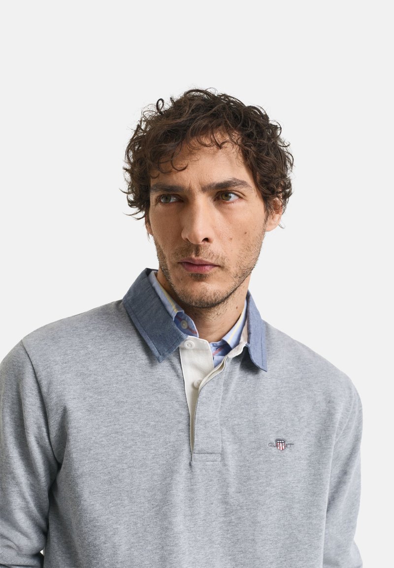 Camisa polo de manga larga gris con un cuello tipo denim, tapeta de botones y logo bordado en el pecho. Textura suave y corte relajado.