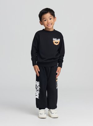 Completo felpa e pantaloni nero con grafica di un orso sul petto e scritta "AWESOME" stampata sui pantaloni, abbinato a sneakers bianche.