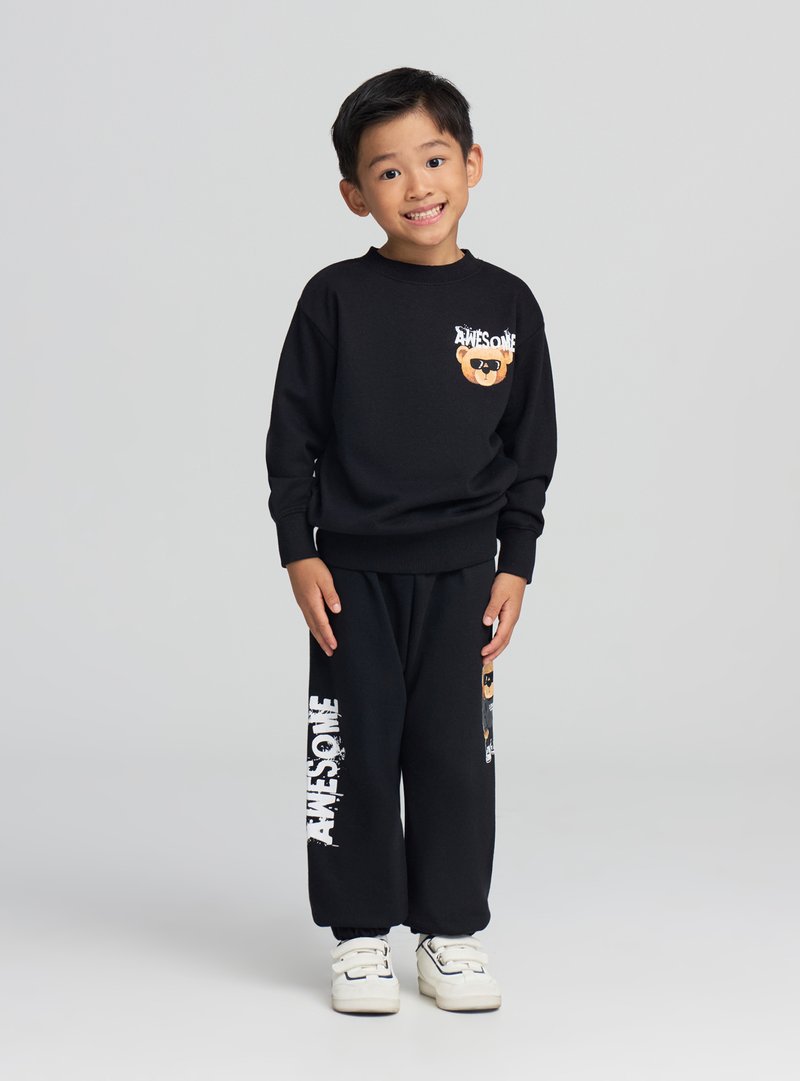 Czarny zestaw z bluzą i spodniami z grafiką niedźwiedzia na piersi oraz napisem "AWESOME" na nogawkach, do tego białe trampki.