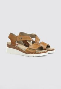 Sandalias de cuero marrón de punta abierta con correas cruzadas, cierres de velcro ajustables y una suela de cuña blanca con costuras decorativas.