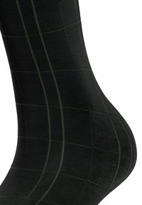 Calza nera alta fino al ginocchio realizzata in materiale morbido, con un motivo a griglia testurizzata e sottili strisce a contrasto.