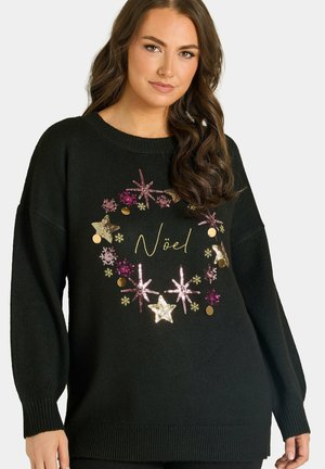 Femme portant un pull noir avec un motif de couronne en sequins rose et or et le mot "Noël" au centre.