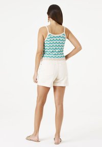 Débardeur en tricot côtelé multicolore avec motif en zigzag, superposé sous un short roulé de couleur crème claire. Texture lisse, bretelles ajustables.