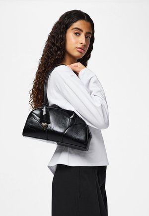 Zwarte leren handtas met een afgeronde vorm, voorzien van een doorgestikte textuur en een metalen accent. Getoond op een model tegen een effen achtergrond.
