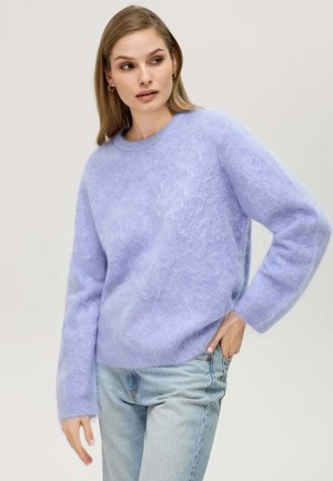 Helle Lavendel, flauschiger Strickpullover mit Rundhalsausschnitt und langen Ärmeln. Getragen mit hellblauen Jeans, die eine lockere Passform und weiche Textur zeigen.